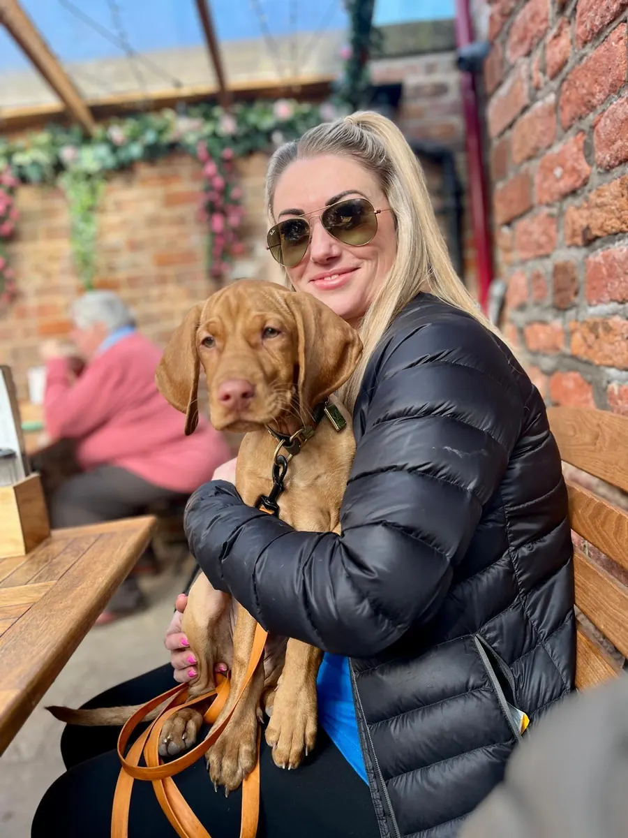 Sarah sitting outside with a young vizsla on her lap